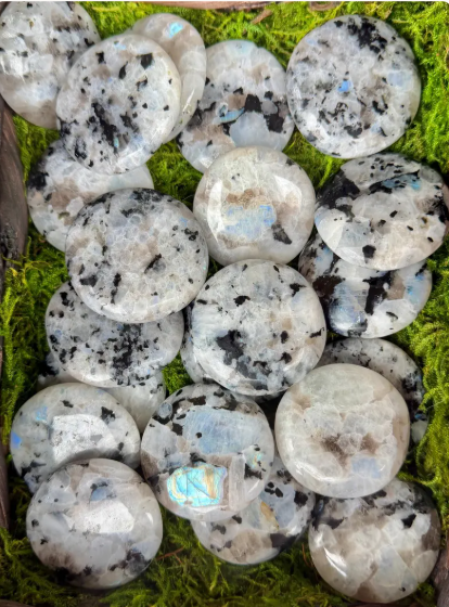 Polished rainbow moonstone palm stones with white tones, dark markings, and colorful flashes on a green background